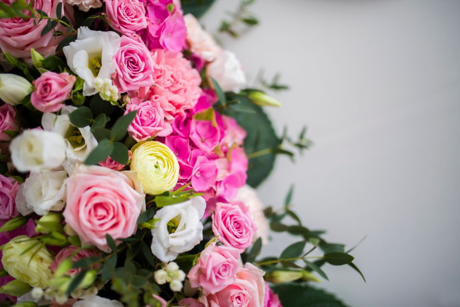 A vibrant floral arrangement featuring a mix of pink, white, and yellow roses, complemented by white lisianthus and green foliage, arranged in a bouquet style. The flowers are fresh with textured peta