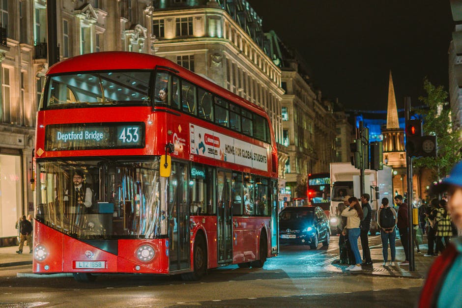 Nighttime scene in Deptford featuring a bright red double-decker bus with the route number 453 displaying 'Deptford Bridge' on its electronic sign. The bus is moving through a busy street illuminated